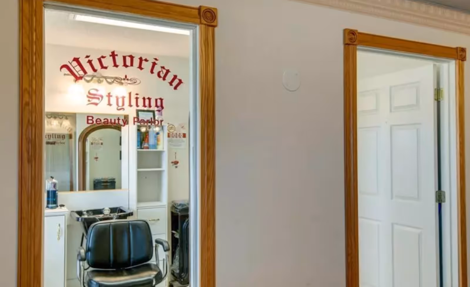 Interior view of a small beauty parlor with a styling chair and sink behind a glass door labeled "Victorian Styling Beauty Parlor."