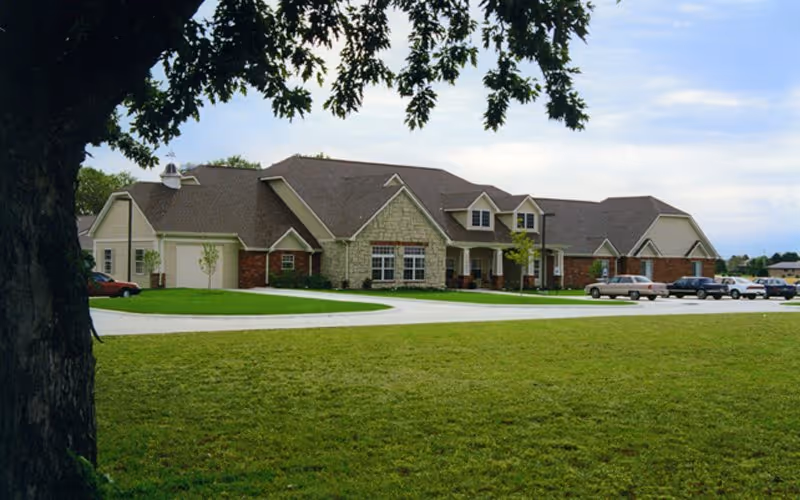 Front exterior of Bickford of Davenport senior living facility with lawn, curved driveway, and parked cars.