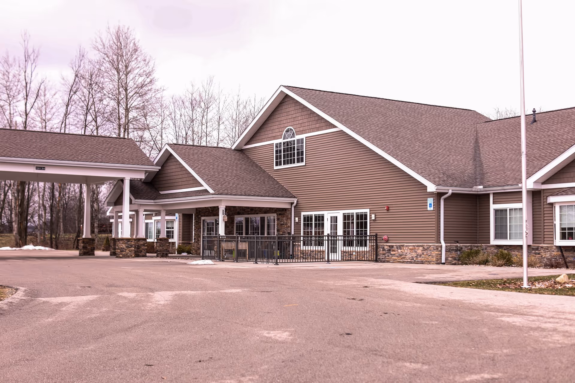 Front exterior of a brown single-story senior living building with a covered entrance and paved driveway.