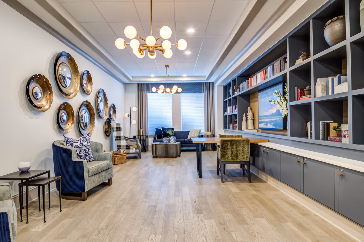 Stylish communal lounge with sofas, armchairs, a long built-in bookshelf wall, and decorative round wall mirrors.