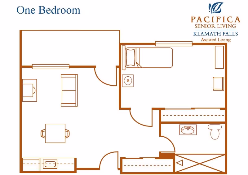 Floor plan of a one-bedroom assisted living apartment at Pacifica Senior Living Klamath Falls, showing a bedroom with a bed and chair, a living area with a sofa and table, a kitchen area with a sink, and a bathroom with a sink, toilet, and shower.