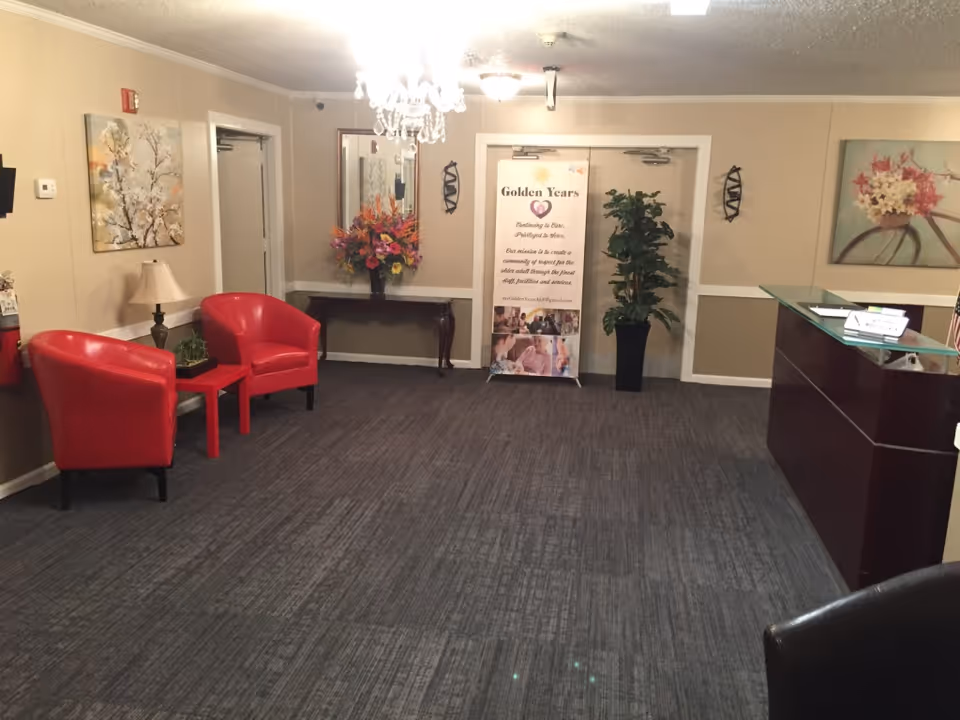 Reception lobby with two red chairs, a small table and lamp, a reception desk, plants, and a 'Golden Years' banner.