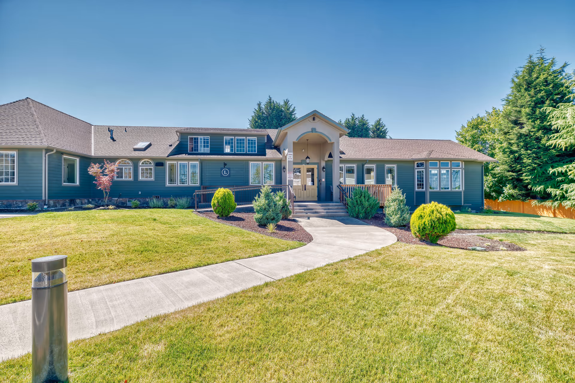 Front exterior of a single-story memory care building with a central entrance, curved walkway, and landscaped lawn.