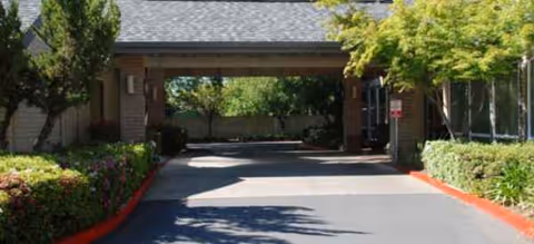 Covered driveway entrance of a senior living facility with landscaped surroundings.