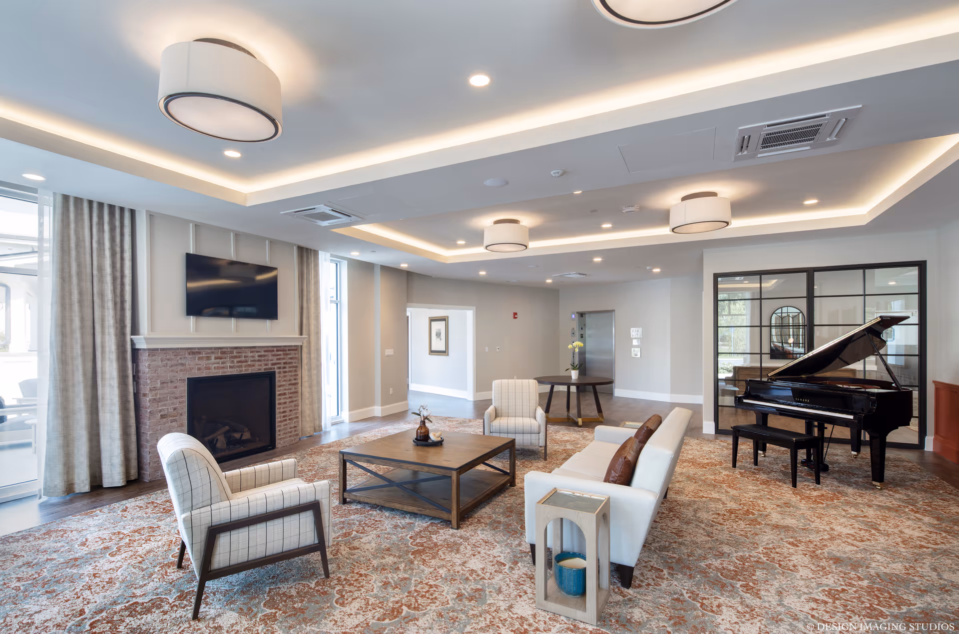 Spacious common room with sofas and chairs around a coffee table, a fireplace and wall TV, and a grand piano.