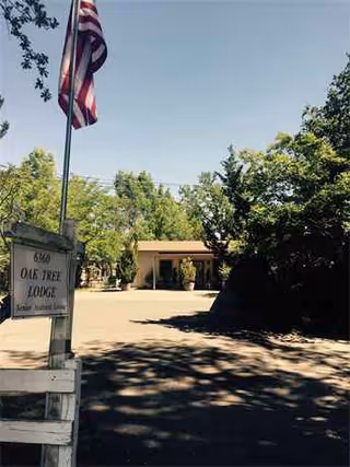 Front view of Oak Tree Lodge entrance with American flag, driveway, and trees.