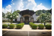 Front exterior view of Marshall Manor Nursing & Rehab Center building with a covered entrance, surrounded by neatly trimmed bushes and trees under a partly cloudy sky.