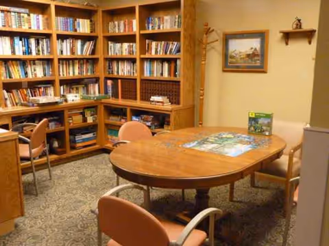 A cozy library in a senior living facility with tall wooden shelves and a round table.