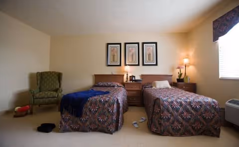 Two twin beds with matching quilts flank a central nightstand in a carpeted bedroom.