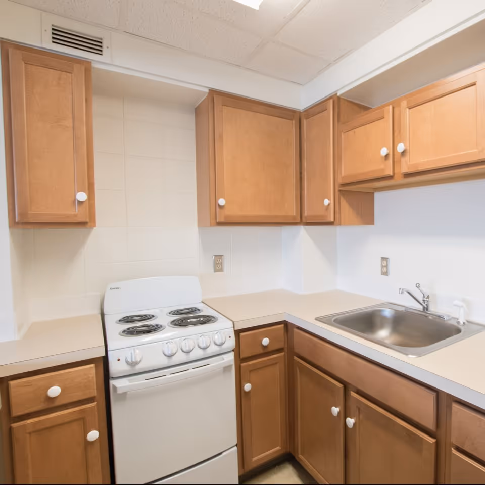 Small kitchen corner with light wood cabinets, an electric stove, countertops, and a stainless steel sink.