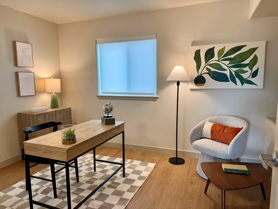 A modern home office nook with desk, chair, rug, floor lamp, and wall art.
