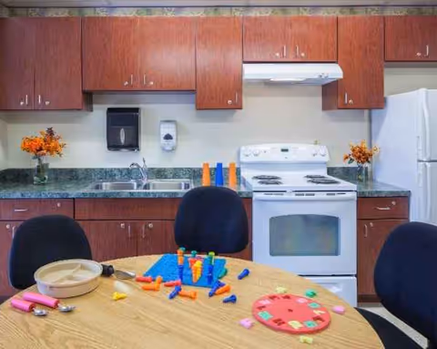 Communal kitchen at Carroll Park Healthcare with wooden cabinets, stove, sink, and a round table.