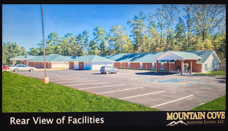 Rear exterior view of Mountain Cove facility with a parking lot and surrounding trees.