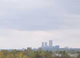 City skyline visible beyond trees under a cloudy sky.