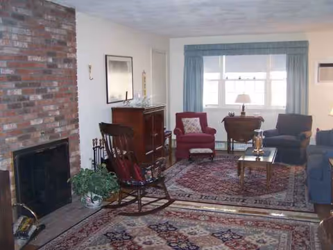 Cozy living room with brick fireplace, seating, and rug in a senior living facility.