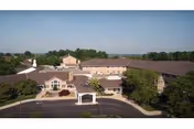 Aerial front view of a multi-wing senior living facility with a covered entrance, circular driveway, and surrounding trees.