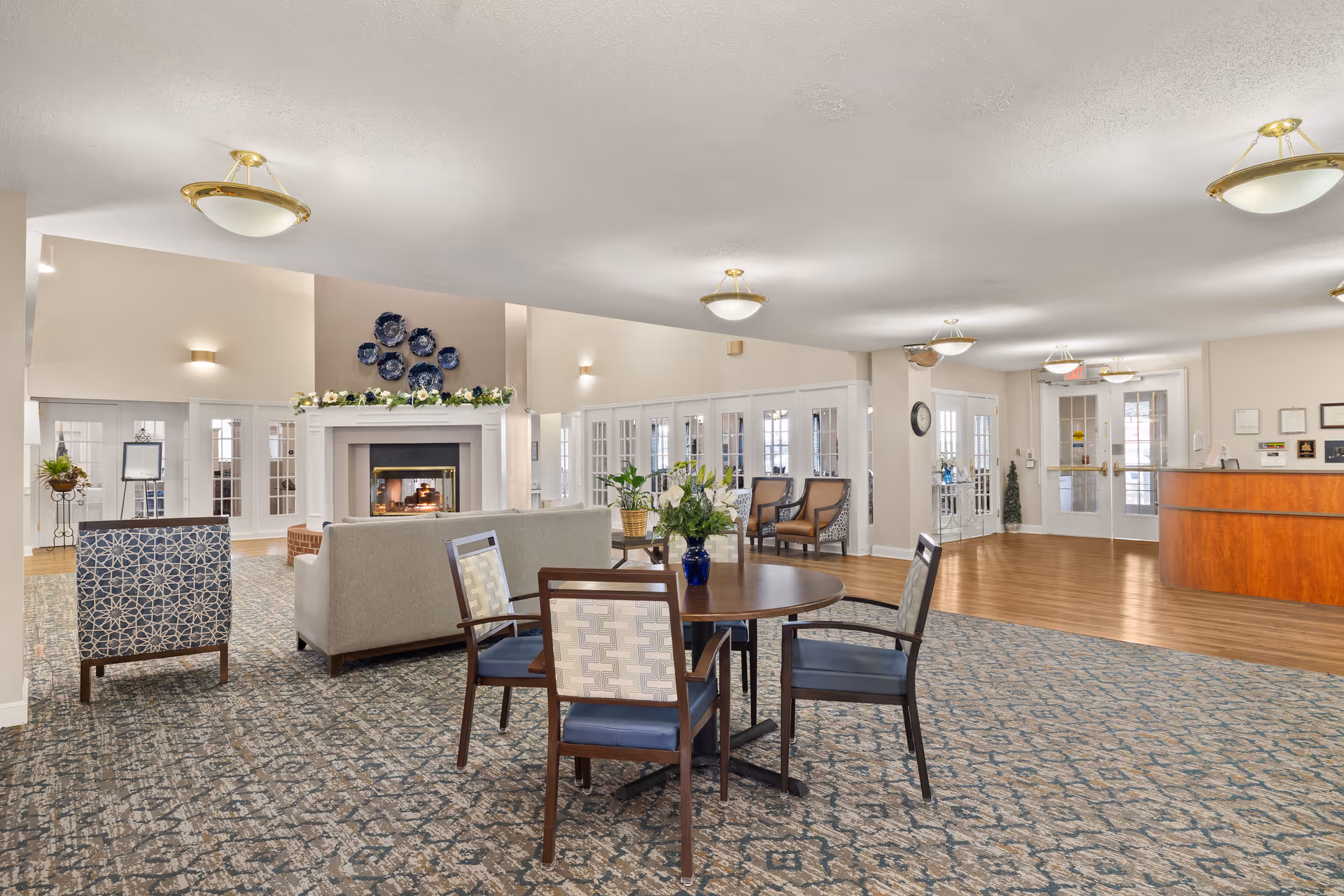 Bright, spacious senior living lobby with seating, a round table, fireplace, and a reception desk.