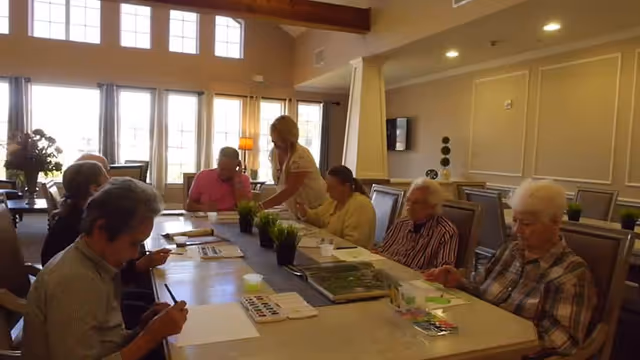 Seniors seated around a long table doing arts and crafts in a well-lit common room.