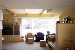 Bright sunlit living room with armchairs, sofa, and shelving in Sunshine Home Care II.