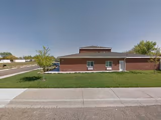 Single-story brick building with a small tree and green lawn in front, under a clear blue sky.