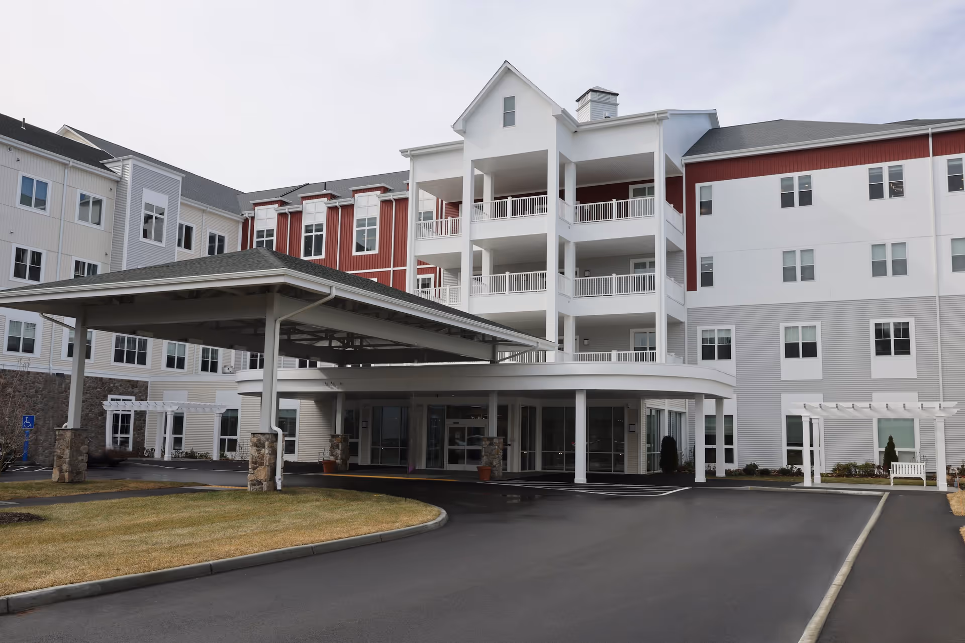 Front exterior view of Whitney Place Assisted Living and Memory Care building with a covered entrance, multiple balconies, and a paved driveway surrounded by grass and landscaping.