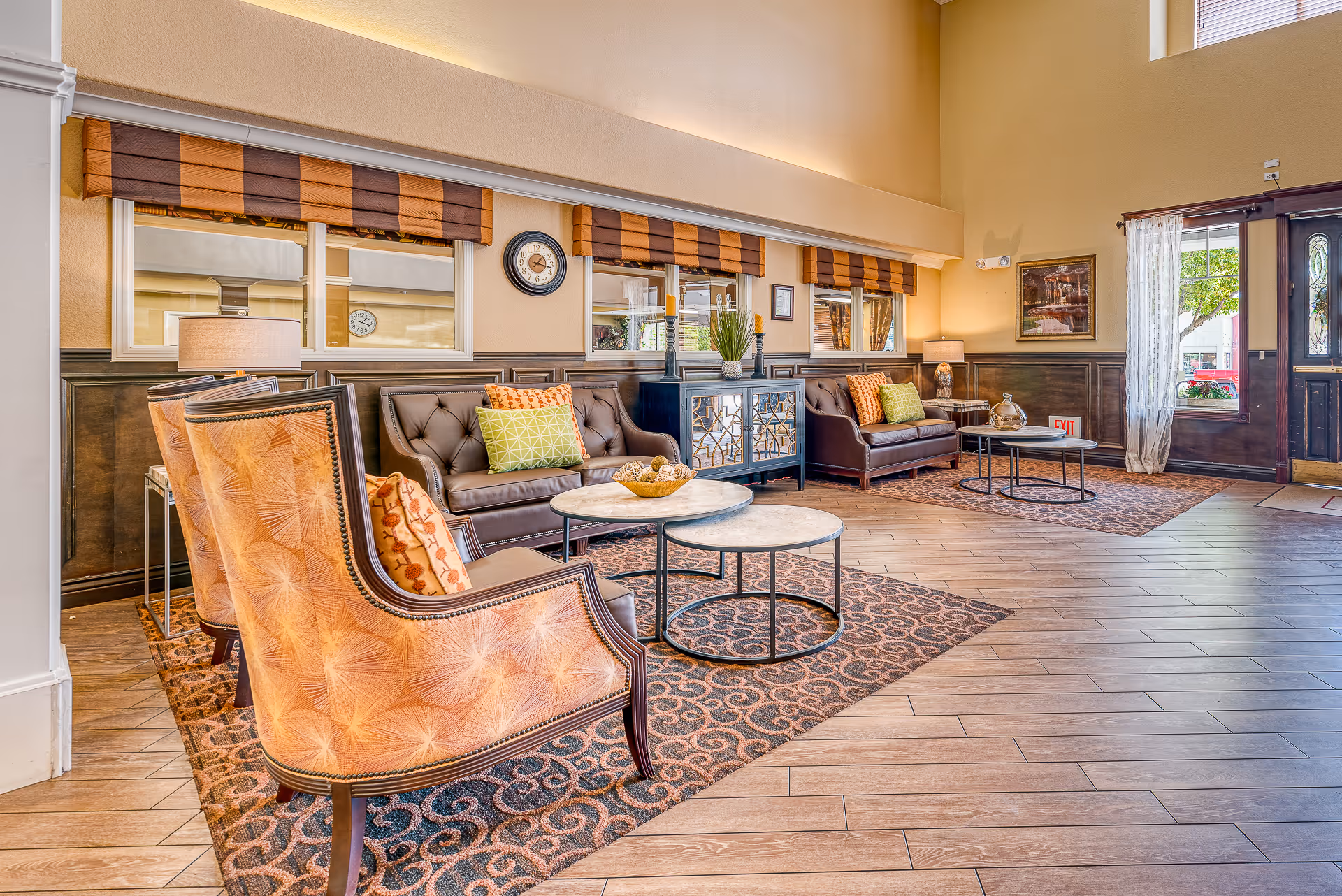 Bright, well-furnished senior living lounge with upholstered armchairs, sofas, nested coffee tables, and decorative accents near the entrance.