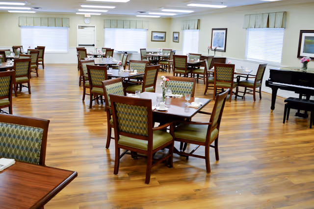 Spacious dining room with multiple wooden tables and green-upholstered chairs set on a wood floor and a piano in the corner.