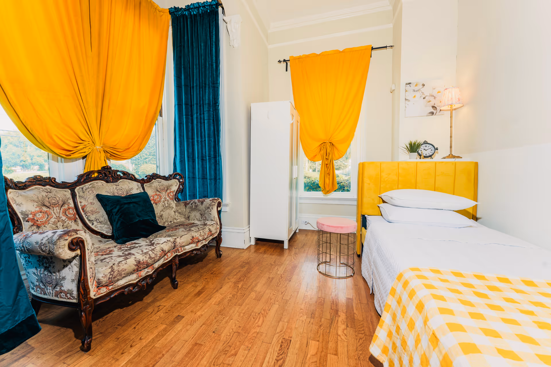 A brightly decorated senior living bedroom featuring a yellow bed, patterned curtains, and a vintage sofa.