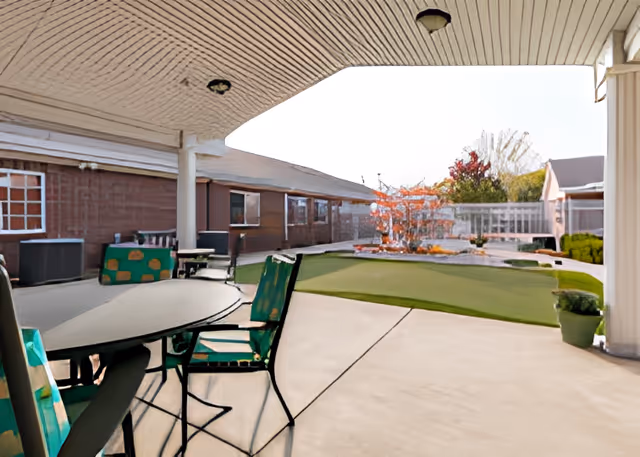 Covered patio seating area looking out onto a courtyard with tables, chairs, and a landscaped lawn.