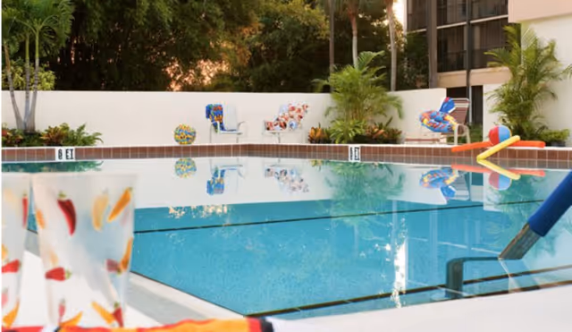 Outdoor swimming pool area with colorful poolside chairs and lush greenery in the background at Village On The Isle facility.