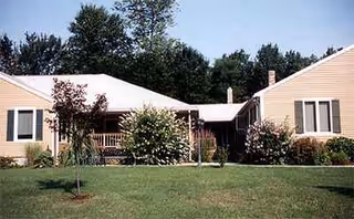 Single-story beige senior living facility with a front porch and landscaped lawn.
