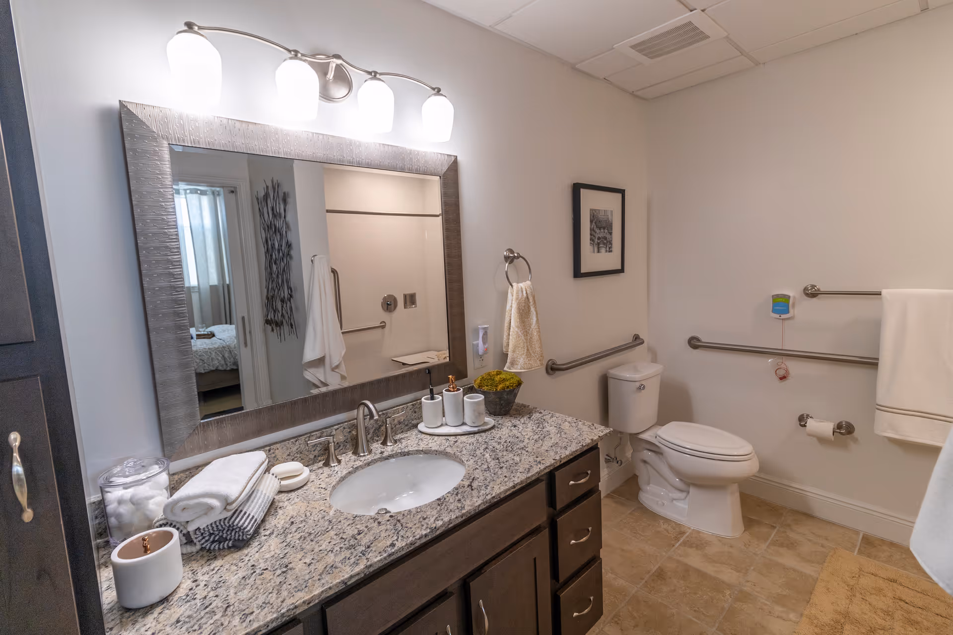 Accessible bathroom with a granite-topped vanity and mirror, sink, toilet with grab bars, and towel rails.