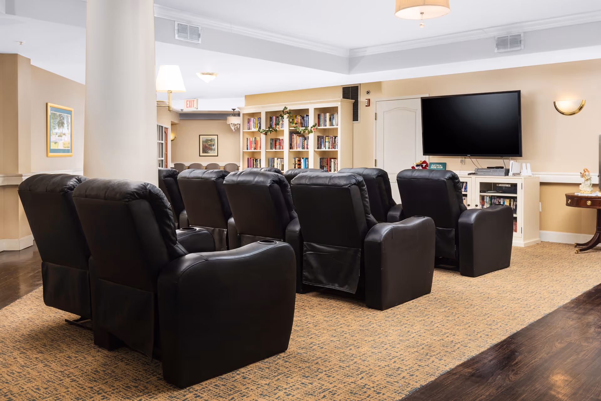 Several black recliner chairs arranged facing a wall-mounted TV in a cozy common lounge with bookshelves.