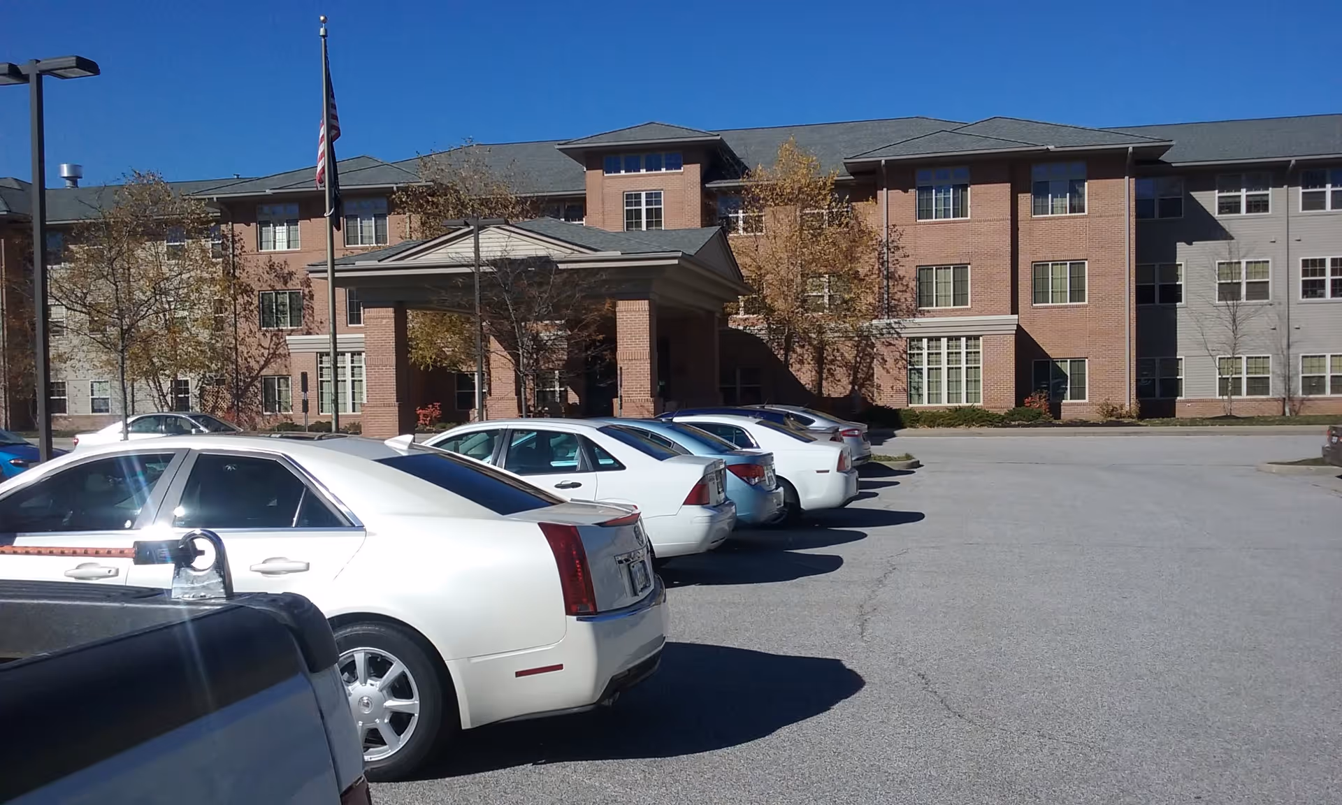 Brick senior living facility with a covered entrance and several parked cars in the front parking lot under a clear blue sky.
