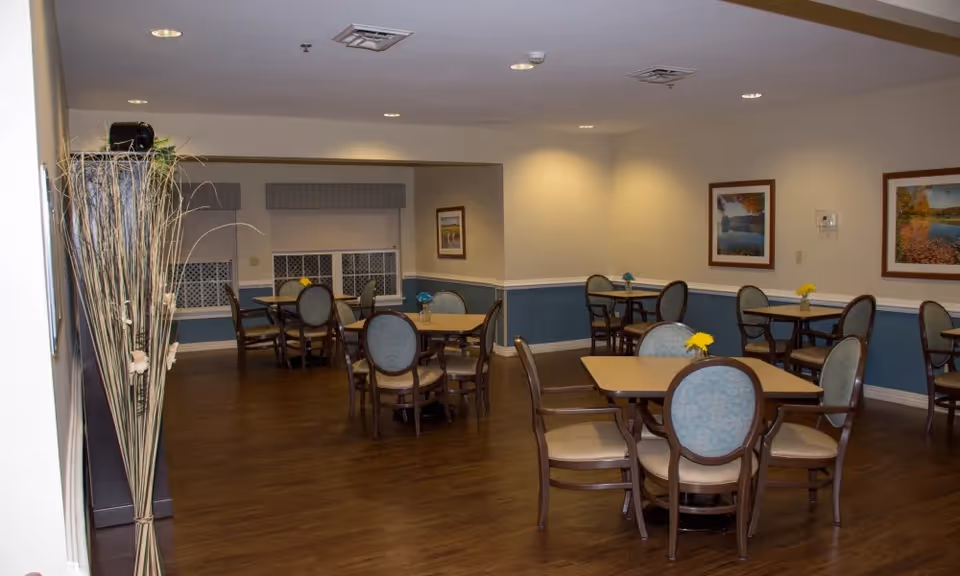 Dining room with multiple round tables and upholstered chairs on wood floors and framed artwork on the walls.