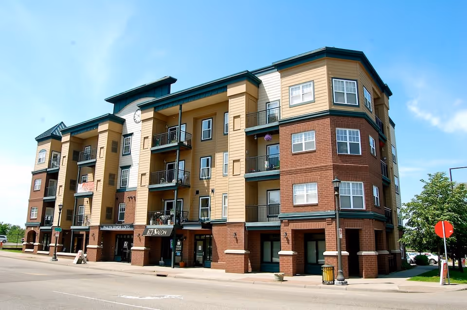 Exterior view of a multi-story senior living apartment building named Phalen Senior Lofts with balconies, a clock on the facade, and a salon on the ground floor under a clear blue sky.