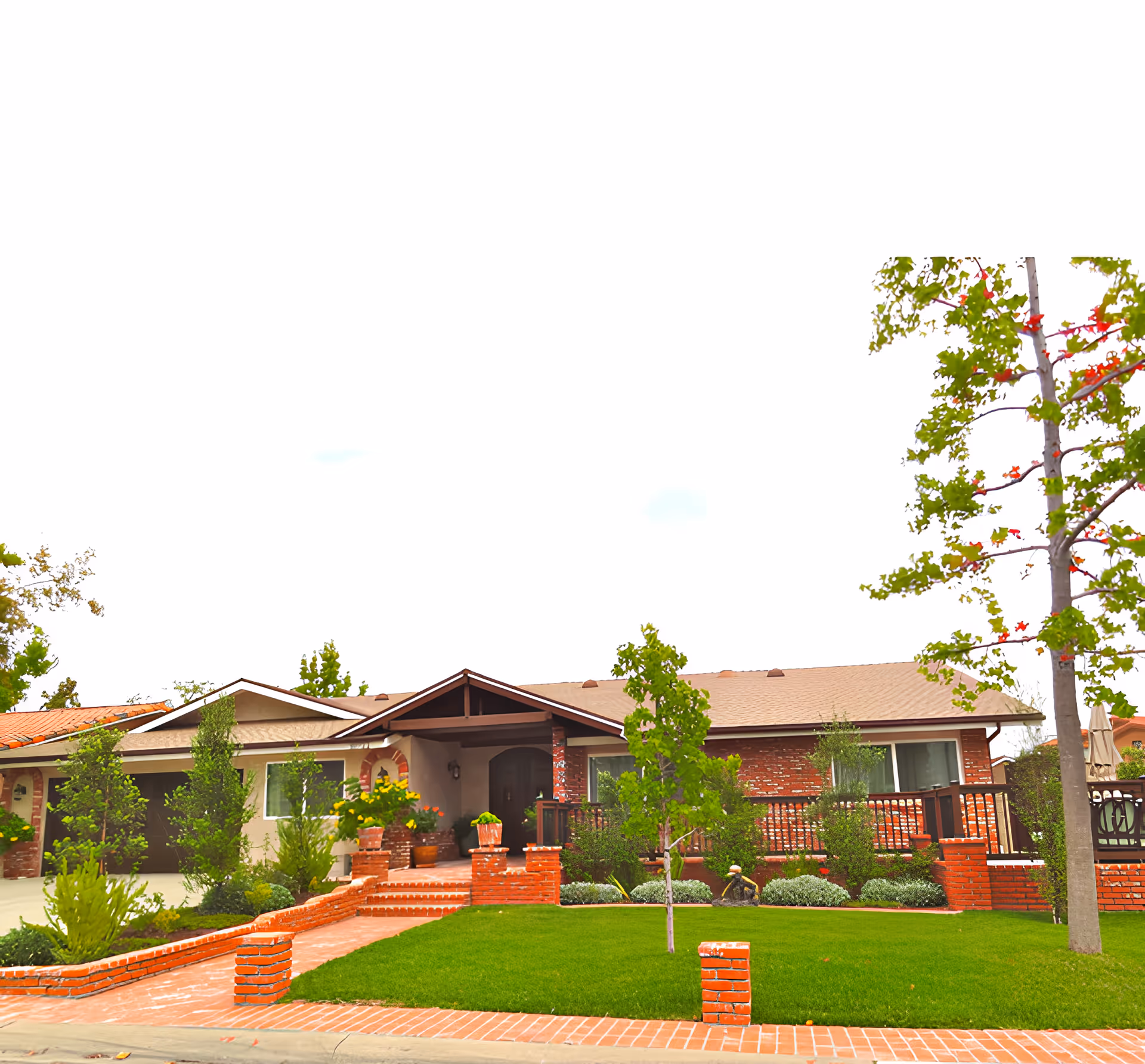 Front exterior view of a single-story residential building with a brick and beige facade, a well-maintained green lawn, several small trees, and a brick walkway leading to the entrance.