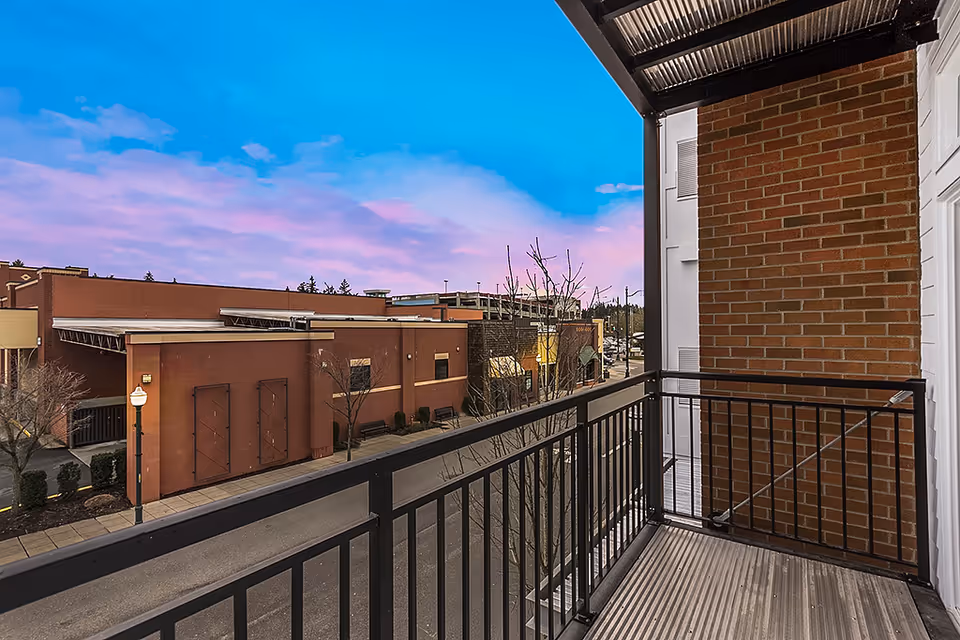 View from a balcony with metal railing overlooking a street and brick buildings under a blue and pink sky at sunset.