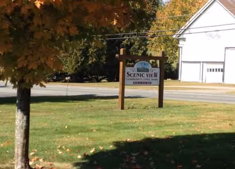 An outdoor grassy area with a Scenic View sign near a road and building.
