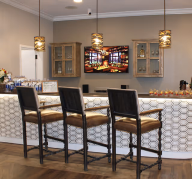 Bar-style seating area with three stools, hanging lights, and a wall-mounted TV.