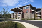 Exterior view of a modern multi-story senior living facility named The Summit, featuring a covered entrance, stone and wood siding, multiple windows, and a curved driveway with landscaping.