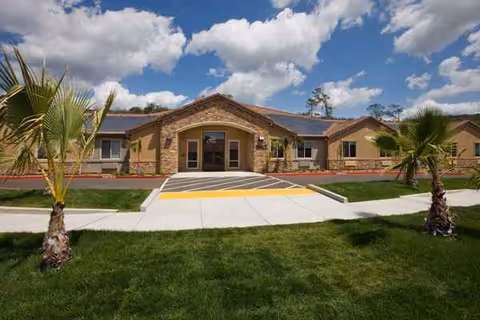 Single-story brick senior living facility with a central entrance, ramp, and palm trees.