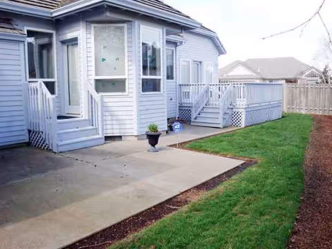 A light blue senior living home exterior with a porch, steps, walkway, and lawn.