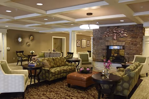 Spacious communal lounge with patterned sofas, armchairs, coffee tables, and a stone fireplace beneath a coffered ceiling.