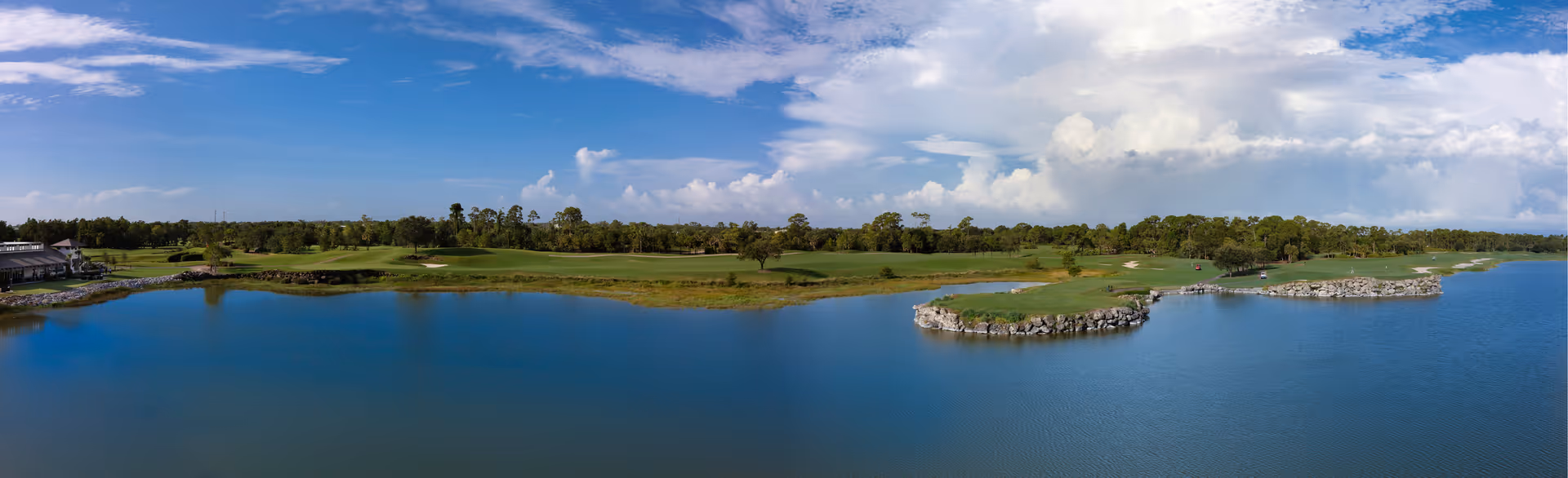 Panoramic view of a large lake with a golf course surrounding it under a partly cloudy blue sky.