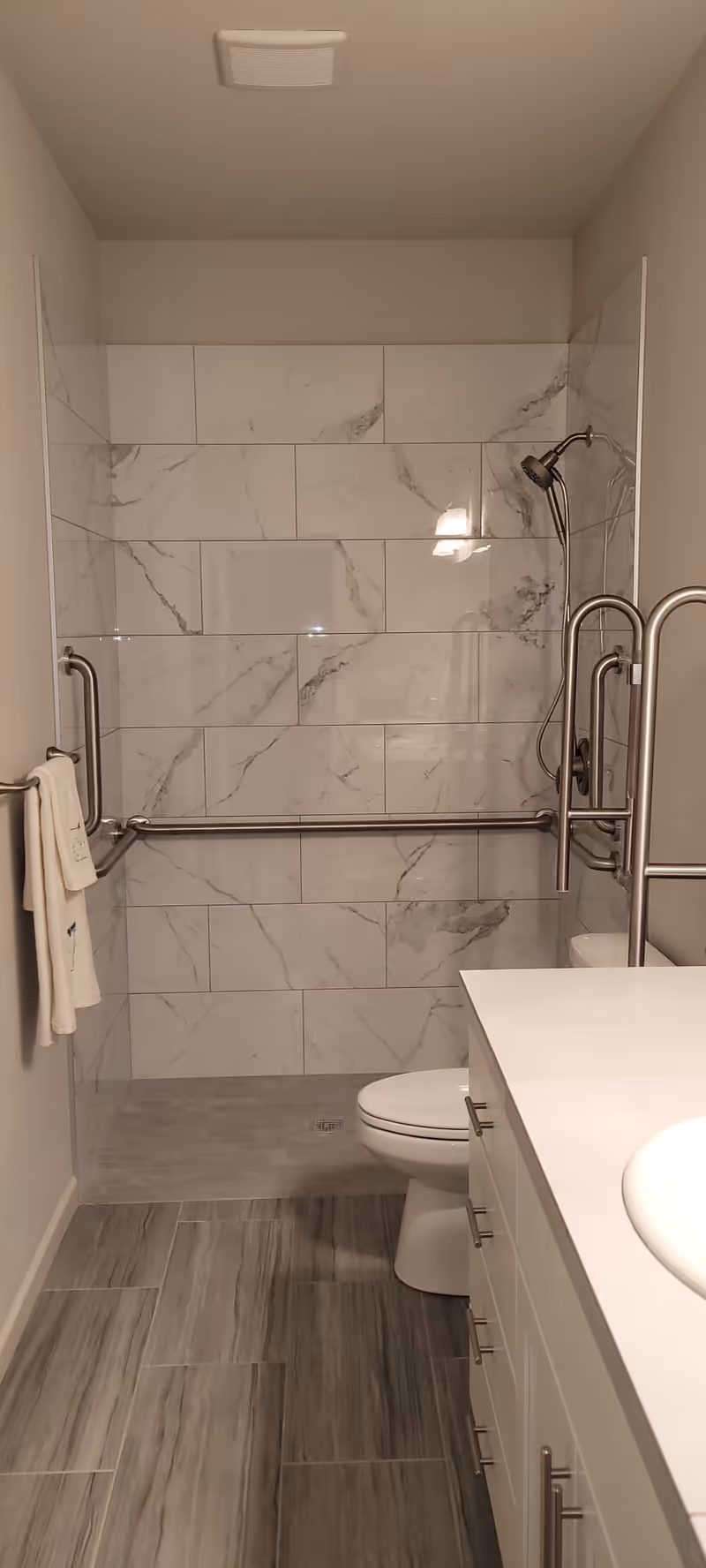 Accessible bathroom with a tiled walk-in shower, multiple grab bars, a toilet, and a vanity countertop.