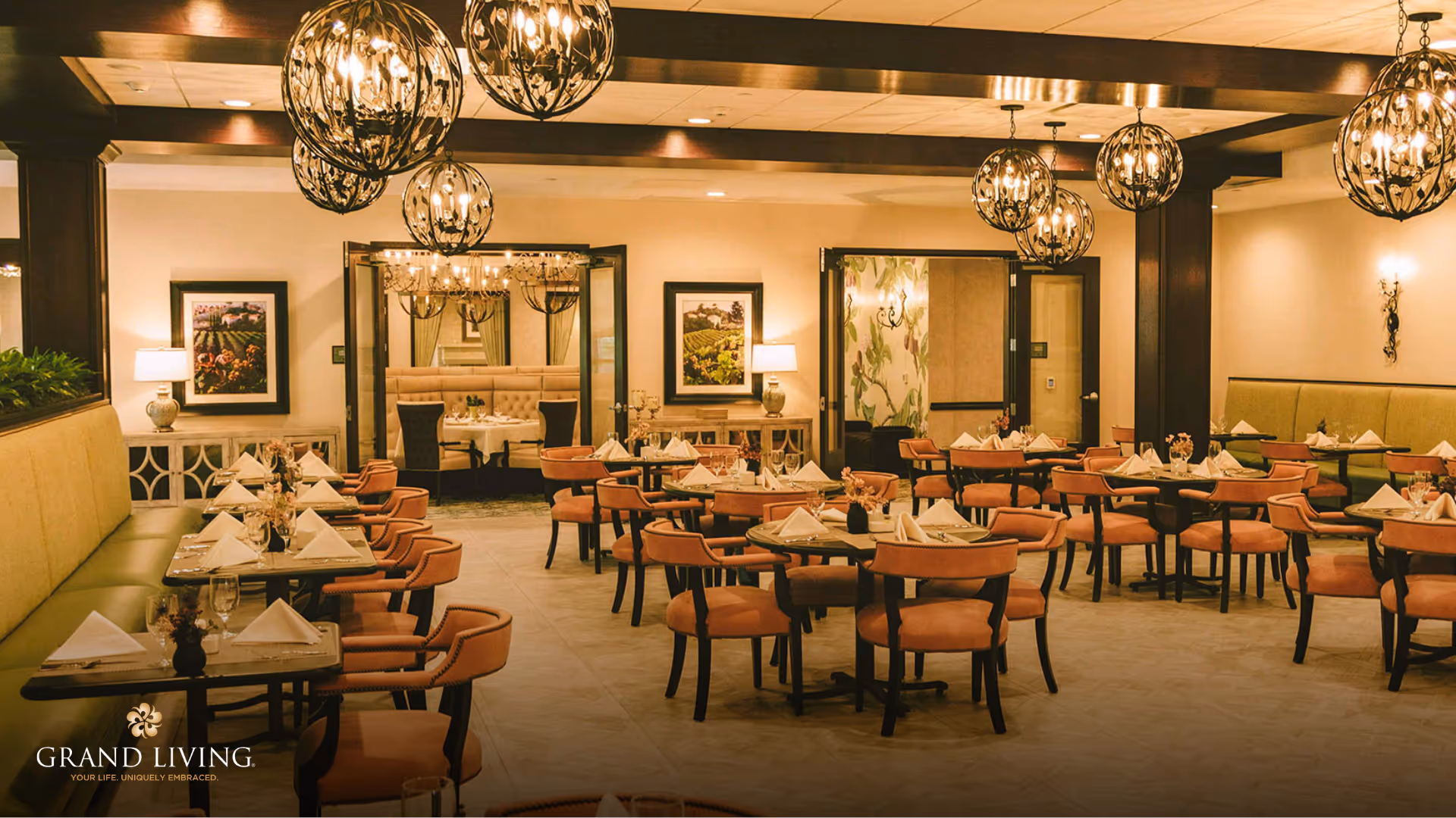 A spacious and elegantly decorated dining room with multiple round and rectangular tables set with white napkins and glassware. The room features warm lighting from spherical chandeliers hanging from the ceiling, green cushioned bench seating along the walls, and framed artwork. There is an adjoining room visible through open double doors with additional seating.