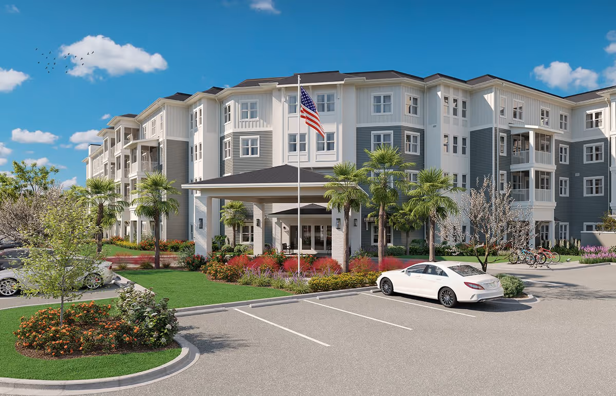 Exterior view of a multi-story senior living facility named Watersound Fountains with a covered entrance, landscaped gardens, palm trees, an American flag on a flagpole, parked cars, and a clear blue sky with some clouds.