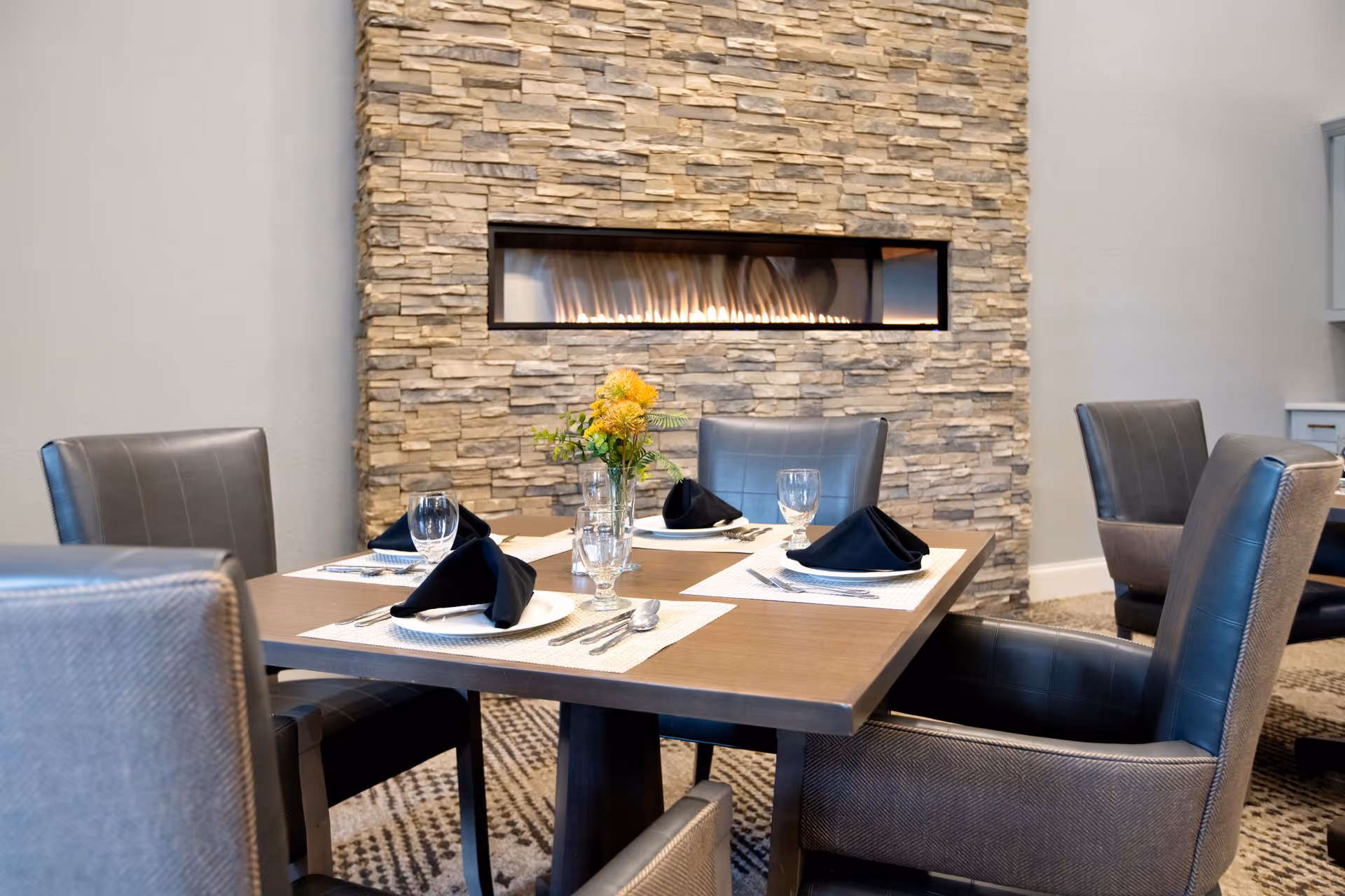 A modern dining table set for four against a stone fireplace wall.