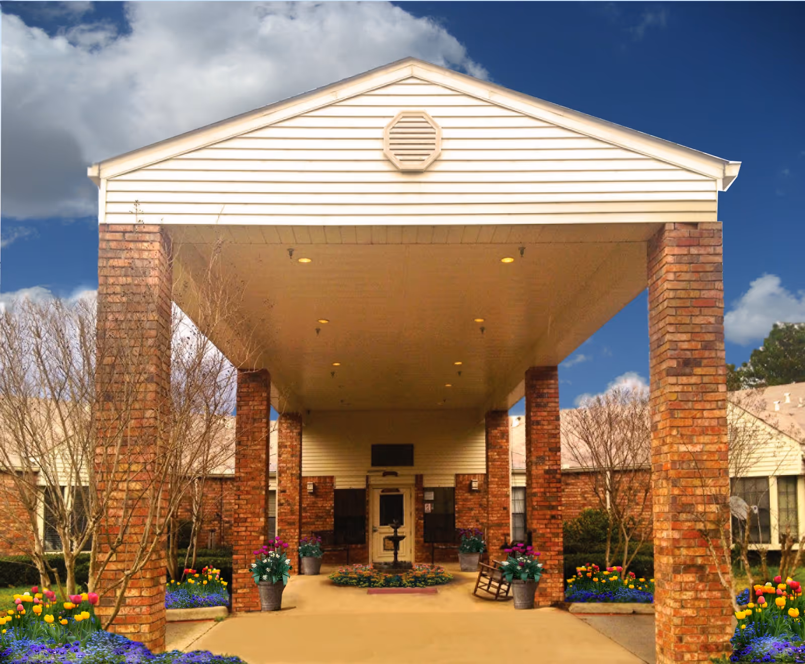 Front entrance of Briarcliff Skilled Nursing Facility with a covered porte-cochere supported by brick columns, potted flowers, and a walkway.